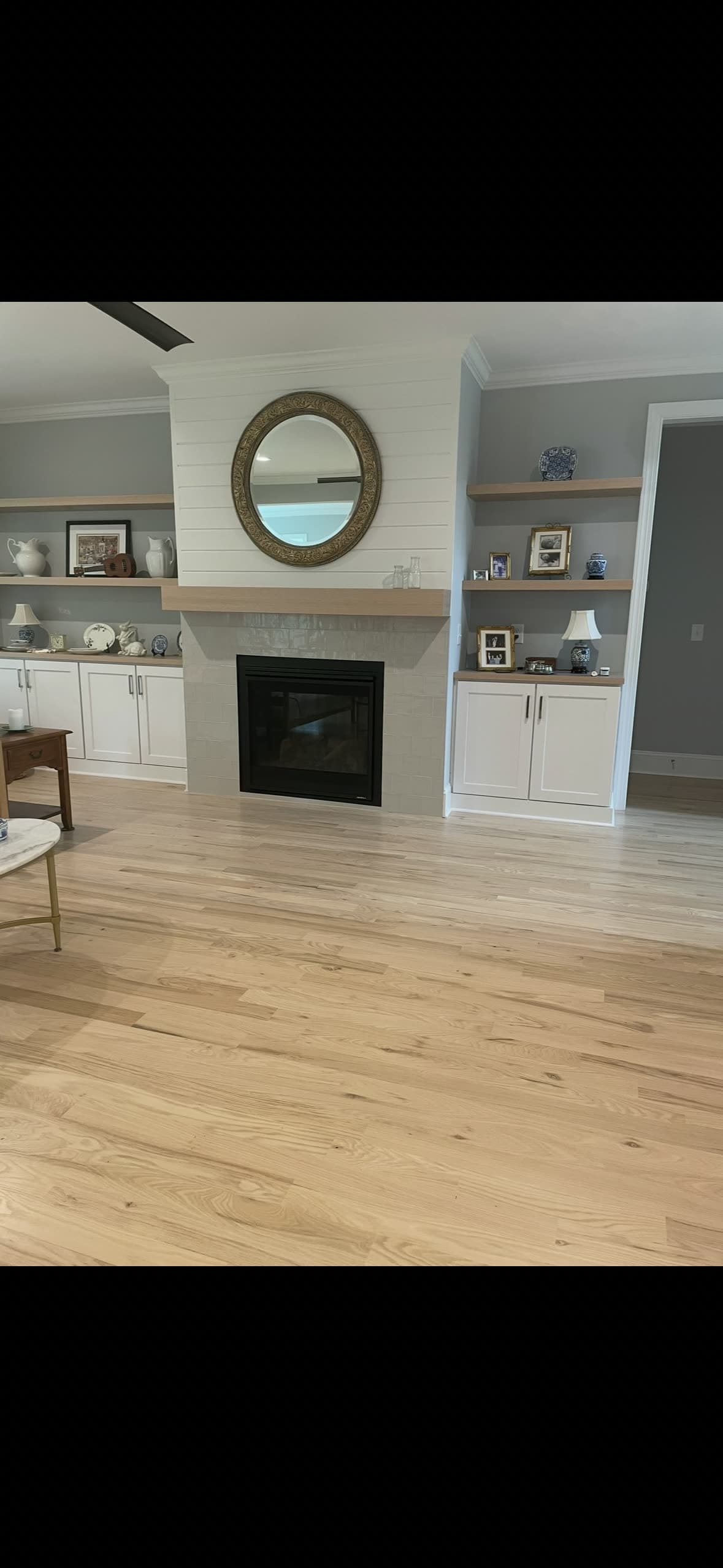 Wide-plank light oak floor in a living room with shiplap fireplace and built-in shelving
