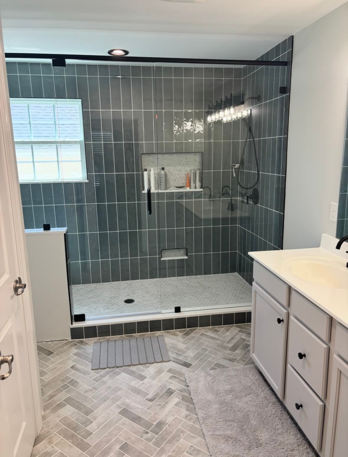 Walk-in shower with vertical-stacked dark tile and herringbone tile floor