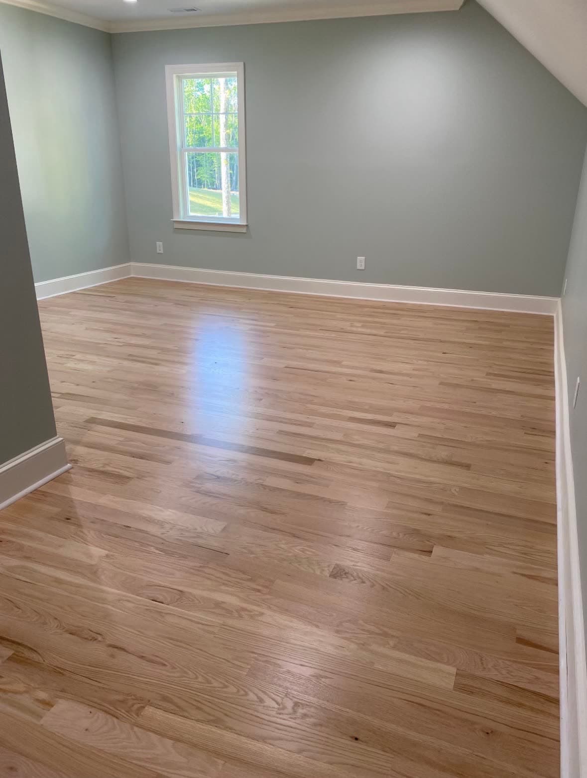 Finished red oak hardwood floor in a freshly painted bedroom with afternoon sunlight